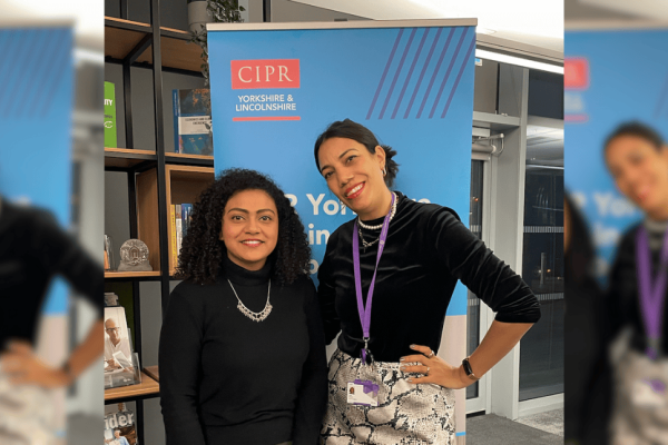A triptych of Teela Clayton and a colleague. Teela is a black woman with short tied back hair wearing a black top and snakeskin skirt. Her colleague is a black woman with mid-length hair wearing a black dress. They are pictured in front of a blue CIP